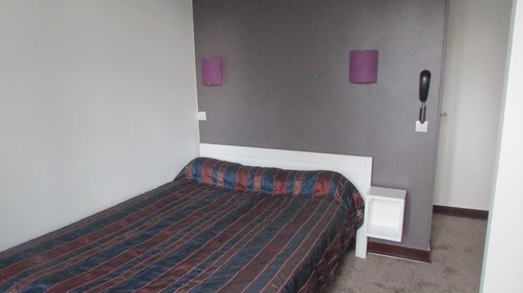 Une chambre à coucher comprenant un lit, des tables de chevet, un téléphone et un luminaire fixé au mur.