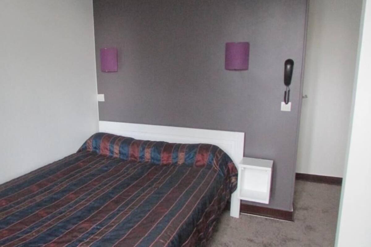 A bedroom with a bed, nightstands, a telephone, and a wall-mounted light fixture.