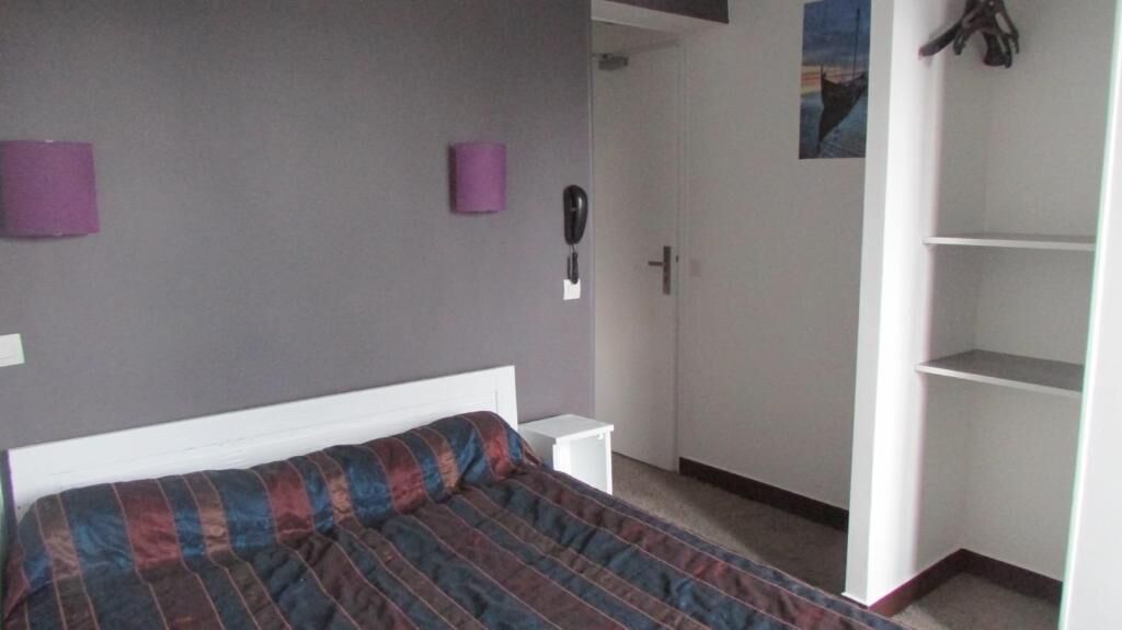 Une chambre à coucher comprenant un lit, une armoire, une table de chevet et un téléphone fixé au mur.