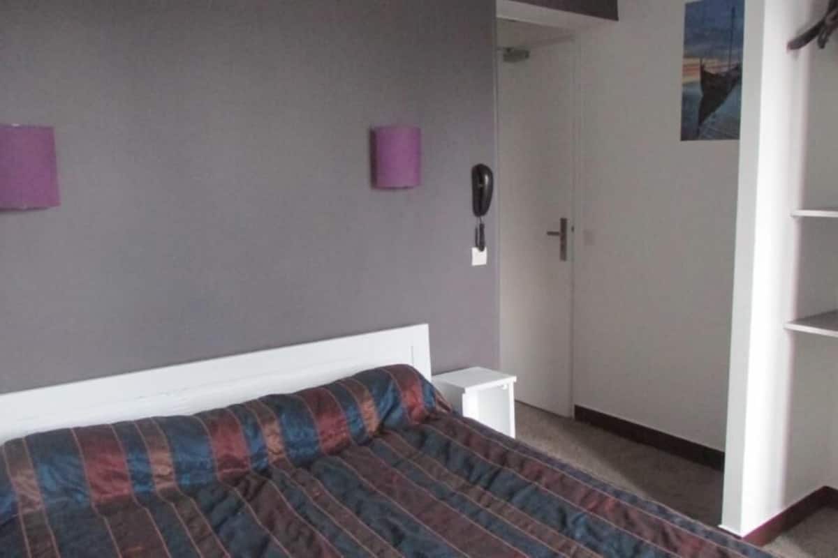 A bedroom with a bed, a wardrobe, a bedside table, and a wall-mounted telephone.
