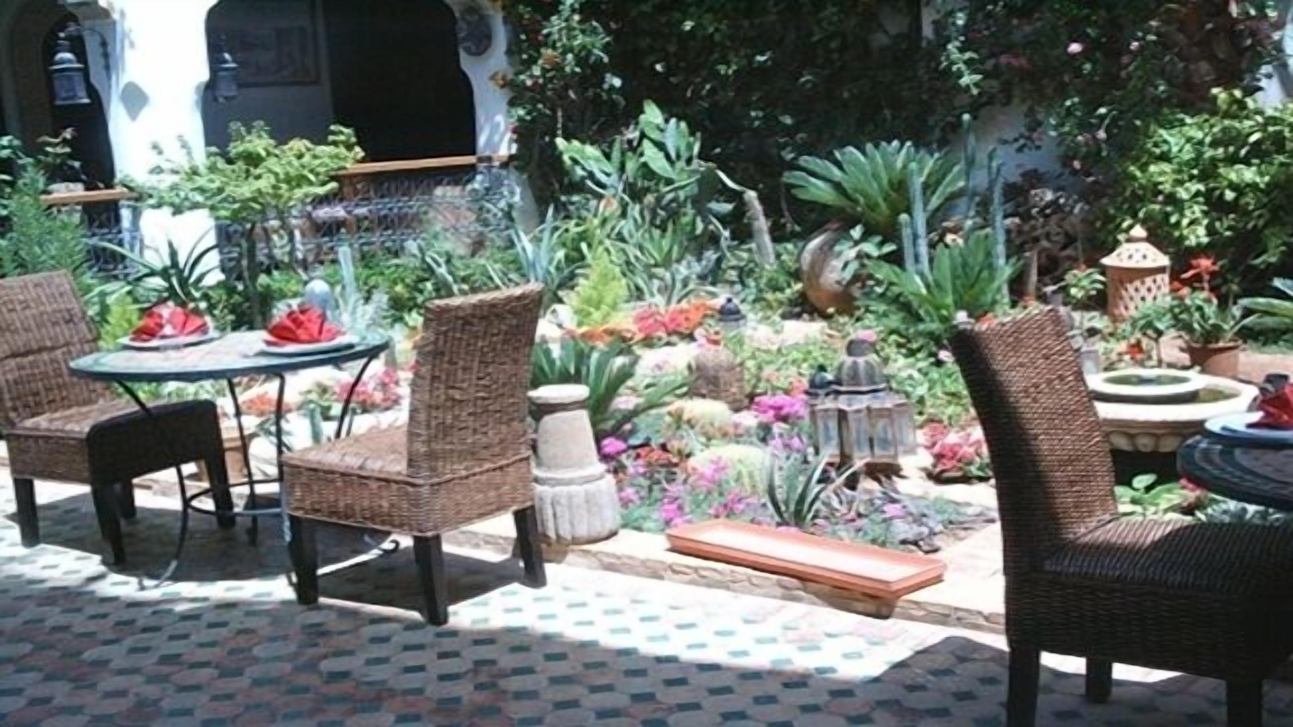 An outdoor seating area with wicker chairs and a table, surrounded by lush greenery and potted plants.