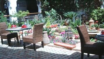 An outdoor seating area with wicker chairs and a table, surrounded by lush greenery and potted plants.