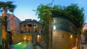 A courtyard with a swimming pool, a covered seating area, and a brick wall with a mural. - Riad Meknès (Meknes)