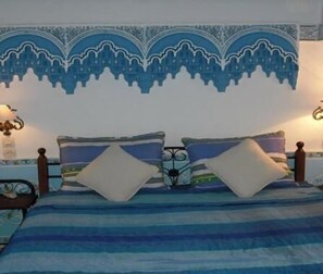 A bed with a striped blue and white bedspread, two pillows, and a decorative wall hanging above. - Riad Meknès (Meknes)