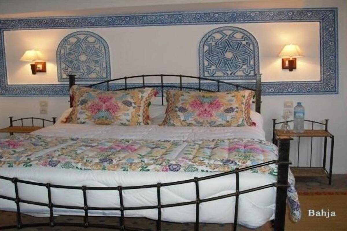 A bed with a floral bedspread, two wall-mounted lamps, and a decorative wall panel.
