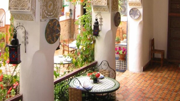 An interior with ornate arches, hanging lanterns, and a small table with a flower arrangement. - Riad Meknès (Meknes)