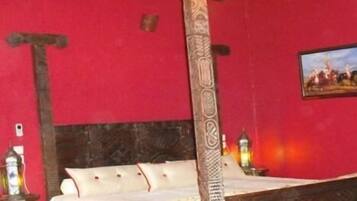 A room with a bed, a wooden bedpost, a red wall, and a painting.