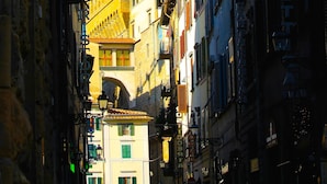 A narrow street with historic buildings, a prominent tower, and a street lamp. - Corte dei Neri (Florence)