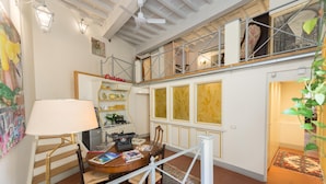 A spacious room with a high ceiling, a staircase leading to an upper level, a dining area with a table and chairs, and a bookshelf filled with books and decorative items. - Corte dei Neri (Florence)