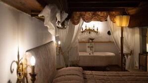 A bedroom with a bed, a chandelier, a vanity with a mirror, and a bathtub. - Corte dei Neri (Florence)