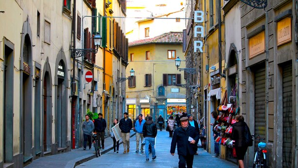 Une rue étroite, bordée de bâtiments des deux côtés, dont certains arborent des enseignes indiquant la présence de boutiques ou d’entreprises.