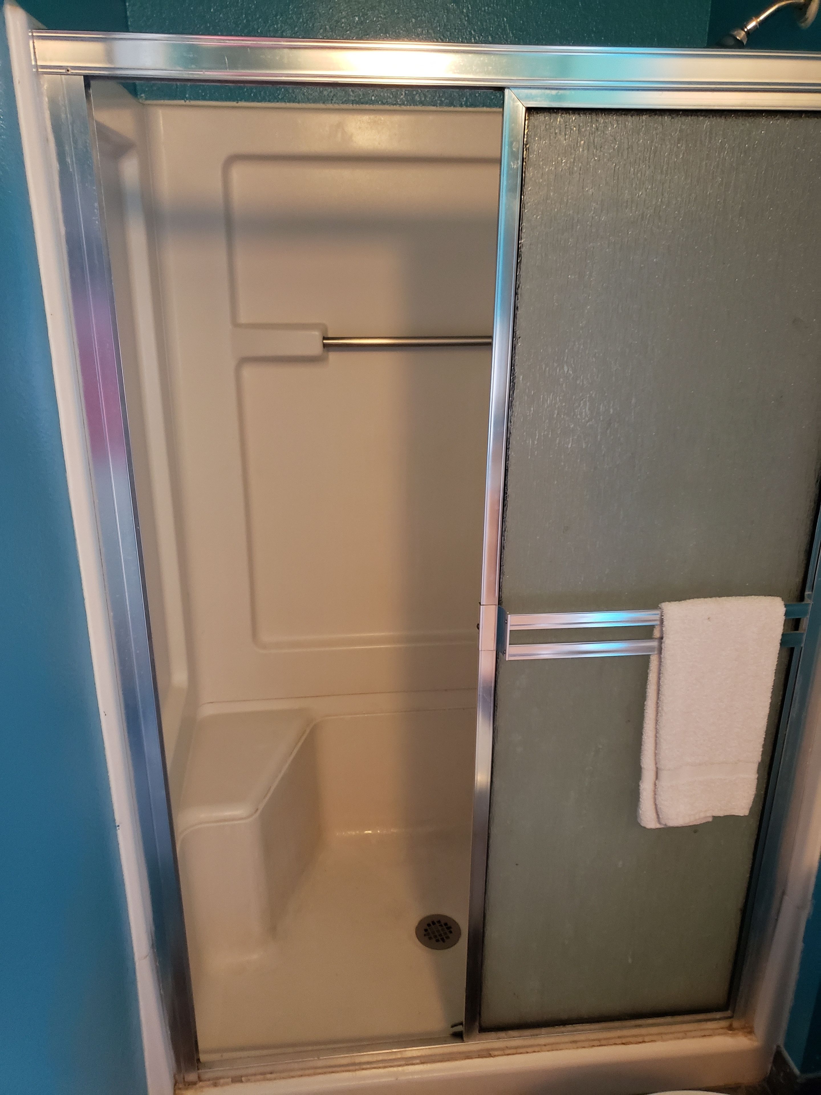 A glass-enclosed shower stall with a towel rack and a visible drain.