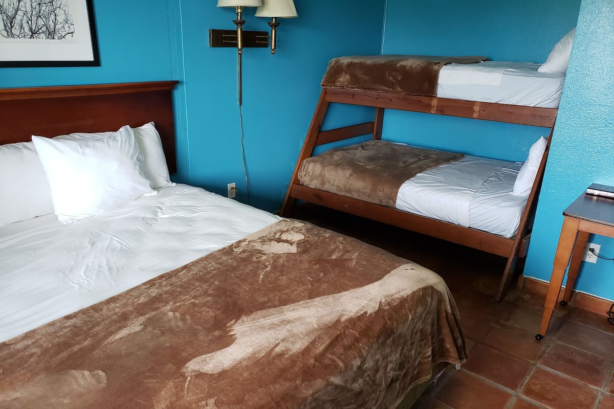 A room with a large bed, a smaller bunk bed, a nightstand, and a wall-mounted lamp.