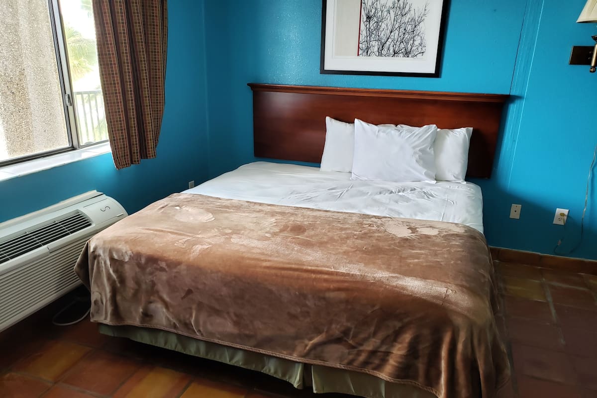 A neatly made bed with a brown bedspread and white pillows in a room with blue walls and a window with curtains.