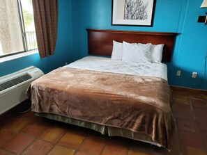 A neatly made bed with a brown bedspread and white pillows in a room with blue walls and a window with curtains. - Hunt's Castle (Rockport)