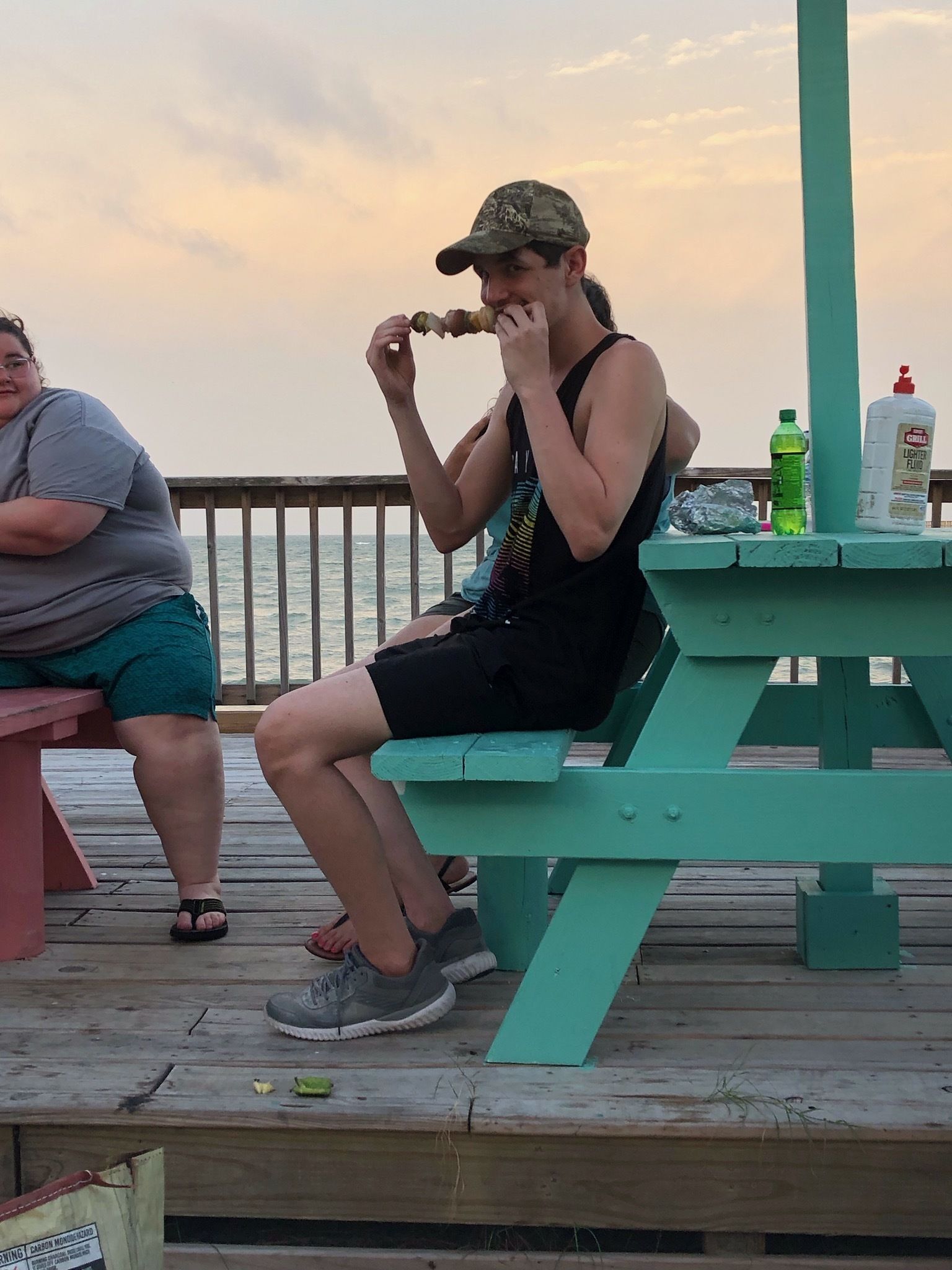 Two people sitting at a wooden picnic table on a pier with a view of the water.