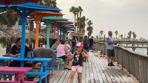 A wooden pier with colorful seating areas and palm trees in the background. - Hunt's Castle (Rockport)