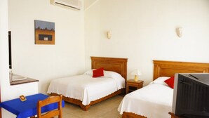 Habitación de hotel con dos camas individuales, un escritorio con silla, televisor y una mesita con lámpara.