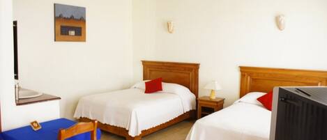A hotel room with two single beds, a desk with a chair, a television, and a small table with a lamp.
