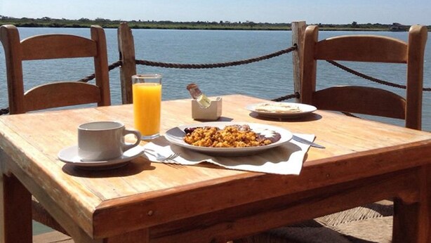 Una mesa de madera con desayuno junto al agua.