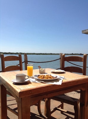 A wooden table with a breakfast setting by a waterfront.
