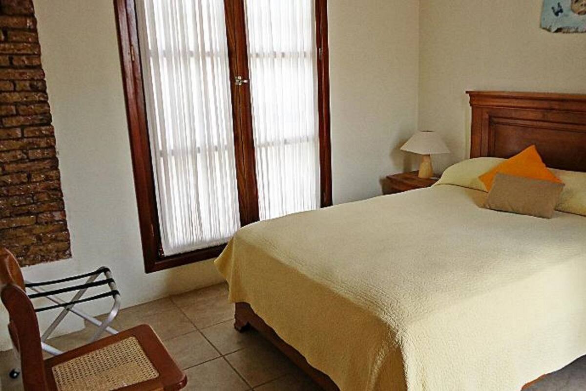 Une chambre à coucher comprenant un lit, une chaise, une table de chevet, une lampe et une fenêtre avec des stores.