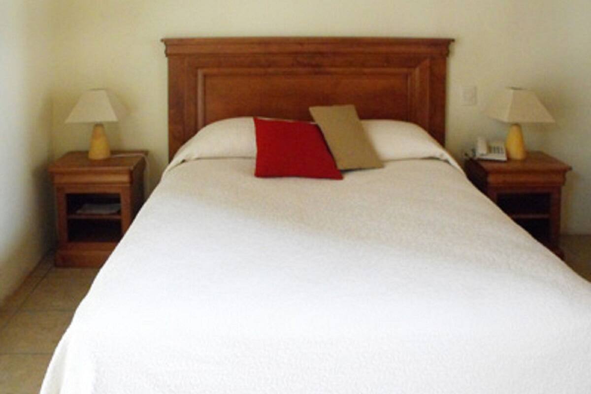 Un lit bien fait, avec une tête de lit en bois, deux tables de chevet avec des lampes et un oreiller rouge.