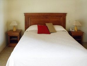 A neatly made bed with a wooden headboard, two bedside tables with lamps, and a red pillow.