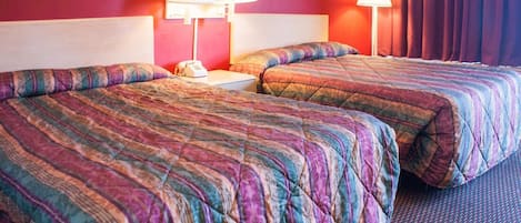 Habitación de hotel con dos camas, cada una con una colcha acolchada de colores, una mesita de noche con lámpara y teléfono.
