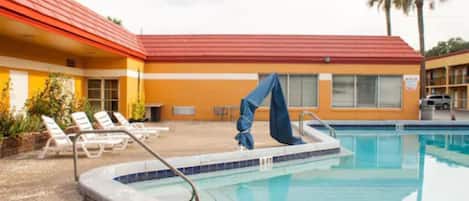 Piscina com espreguiçadeiras e área coberta, anexa a um edifício com telhado vermelho.