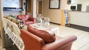 A lobby with leather sofas, a coffee table, a reception desk, and a TV screen. - Scottish Inn Jacksonville Downtown (Jacksonville)