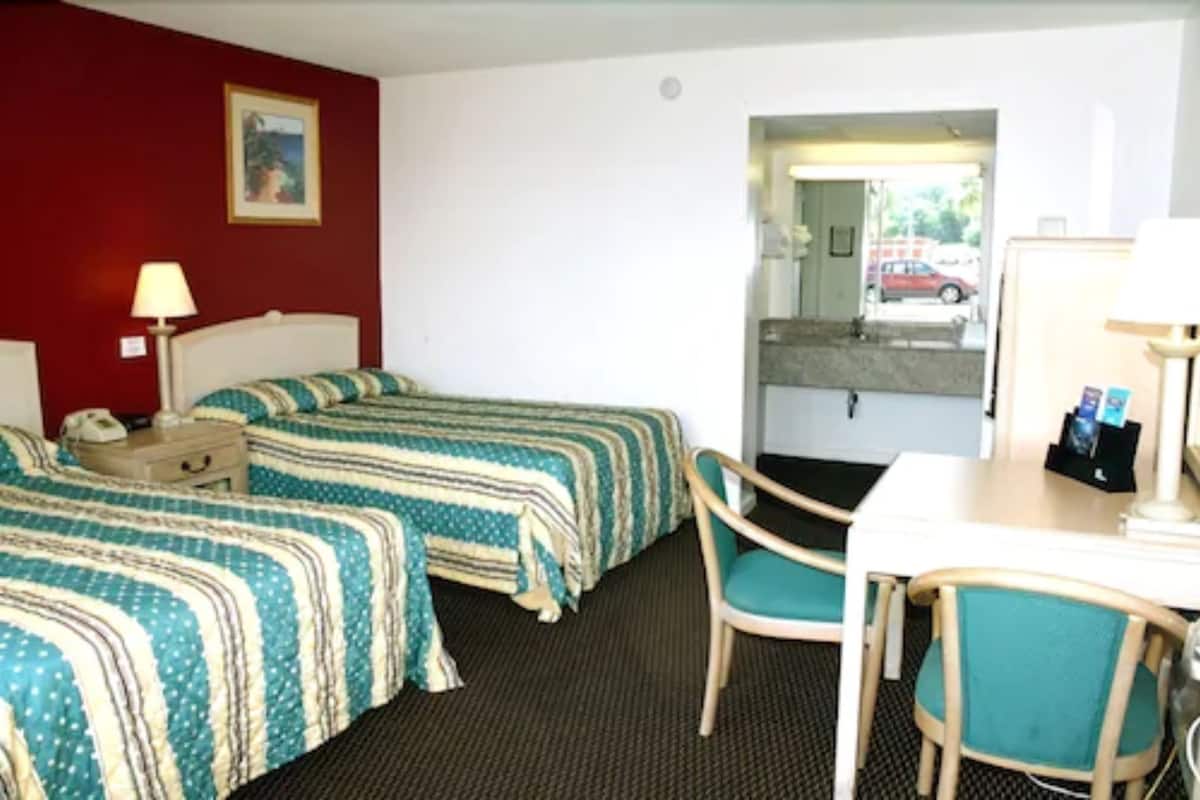 A hotel room with two beds, a desk, a chair, a lamp, a telephone, and a painting on the wall.