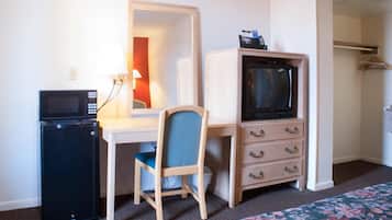 Une chambre d’hôtel de taille modeste, équipée d’un bureau, d’une télévision, d’un petit réfrigérateur, d’une chaise et d’une armoire.