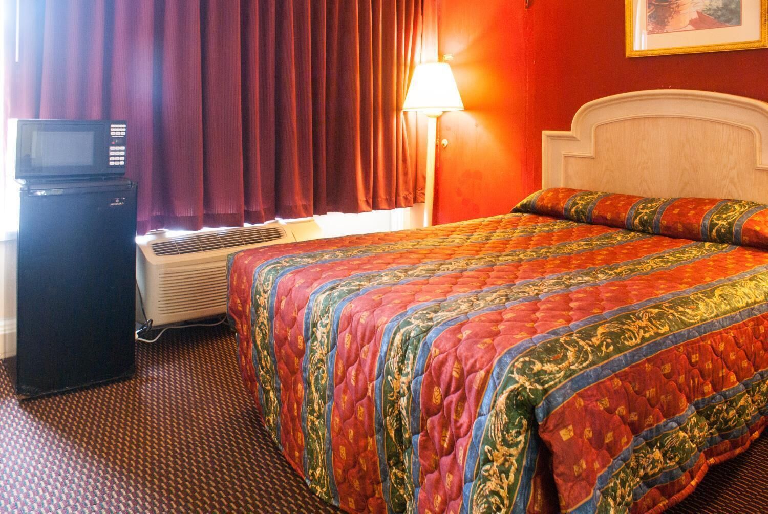 Een hotelkamer met een bed, een televisie, een airconditioner en een lamp.