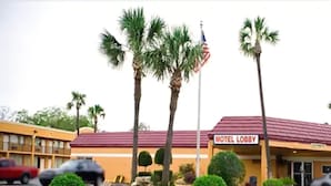 A motel lobby with a red roof, palm trees, and an American flag. - Scottish Inn Jacksonville Downtown (Jacksonville)