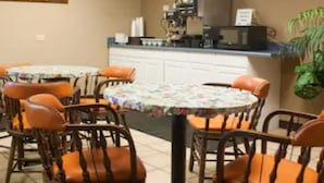 A dining area with round tables and wicker chairs, a kitchen counter, and a potted plant. - Scottish Inn Jacksonville Downtown (Jacksonville)