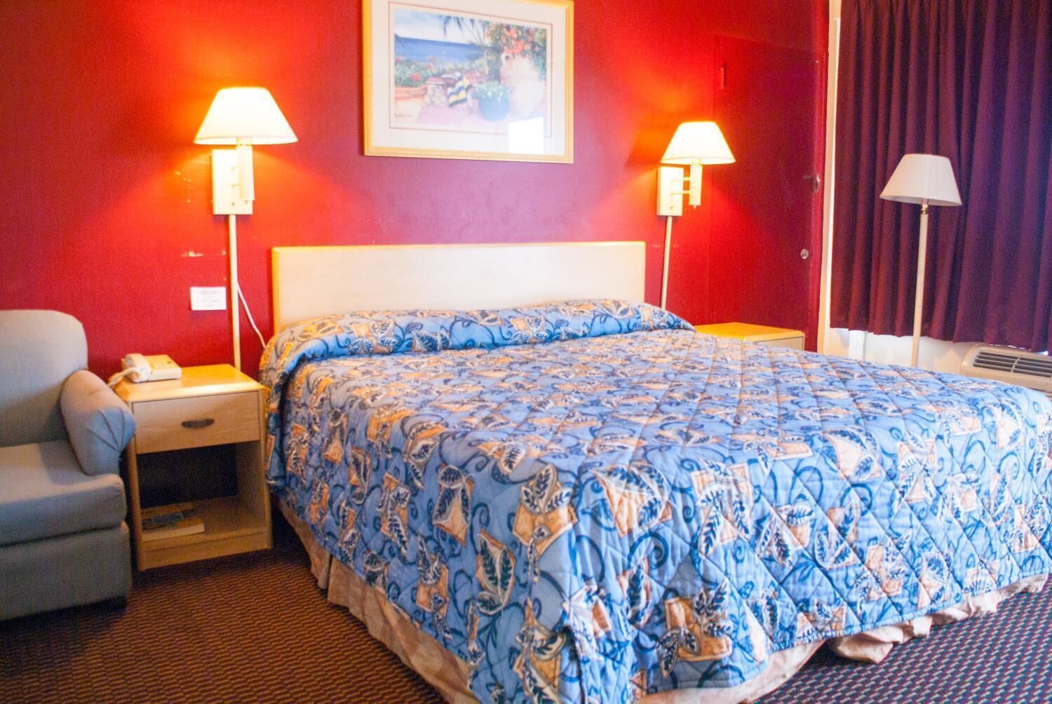 A hotel room with a large bed, two bedside lamps, a chair, and a painting on the wall.