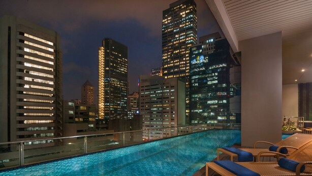 A rooftop pool with a cityscape view, wooden deck, and lounge chairs.