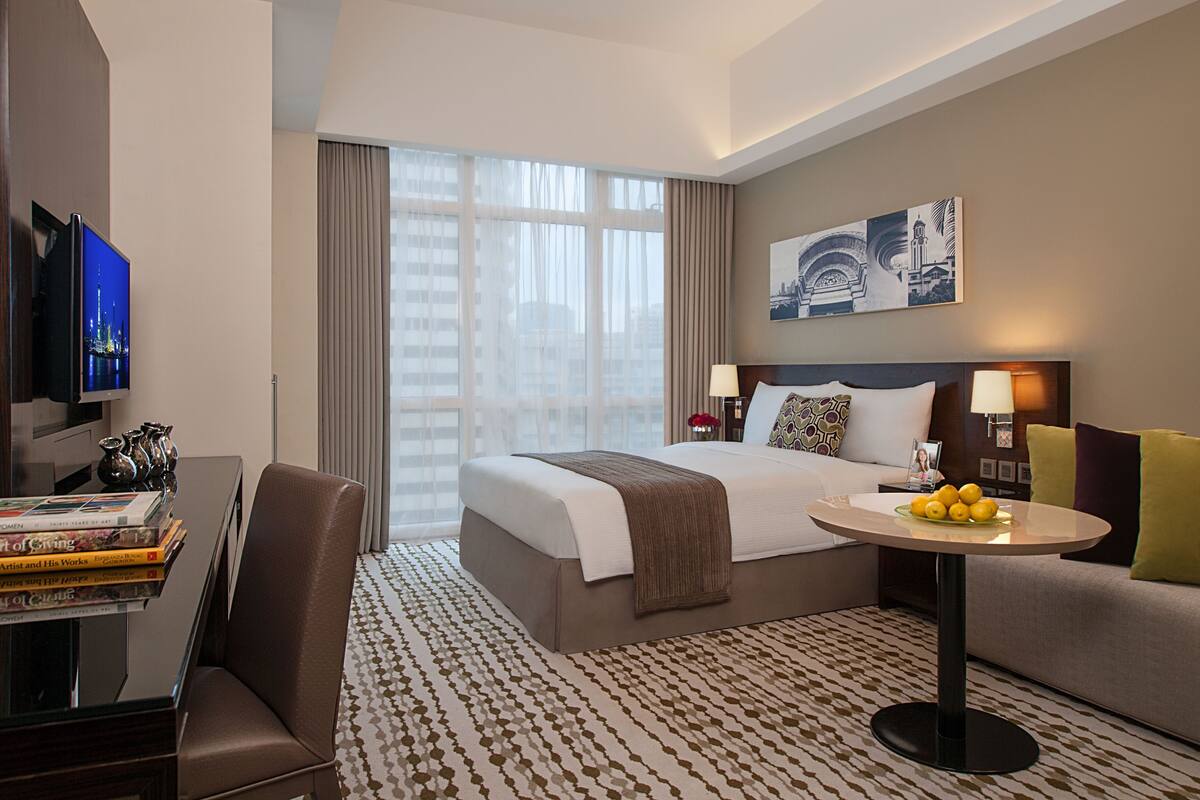 A hotel room with a bed, a desk with a TV, a coffee table with lemons, and a couch.