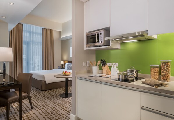 Habitación de hotel con cama, mesita de noche, lámpara y vistas a la ciudad. La habitación cuenta con una kitchenette equipada con microondas, estufa y varios utensilios de cocina.