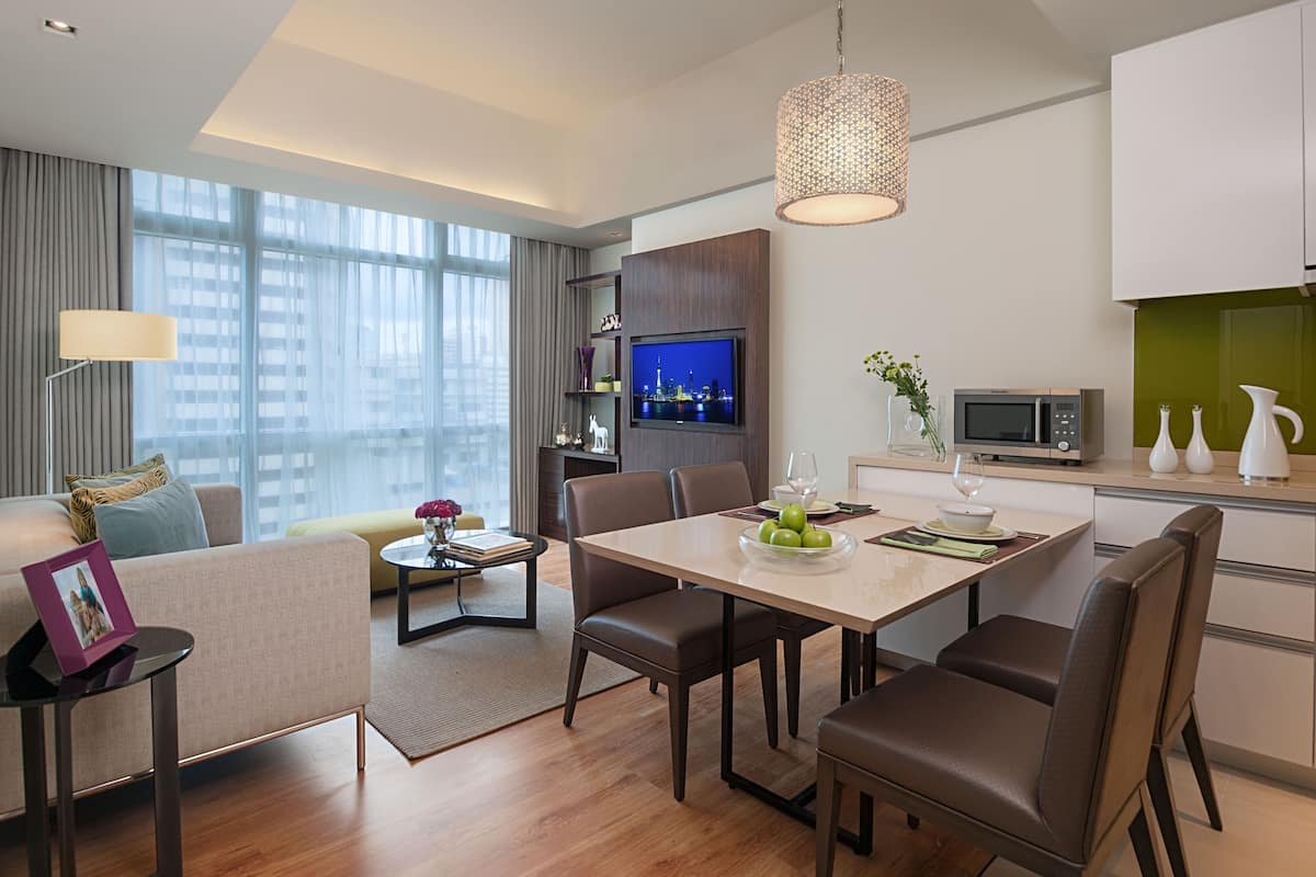 A modern hotel room with a dining area, a sofa, a TV, and a kitchen area.