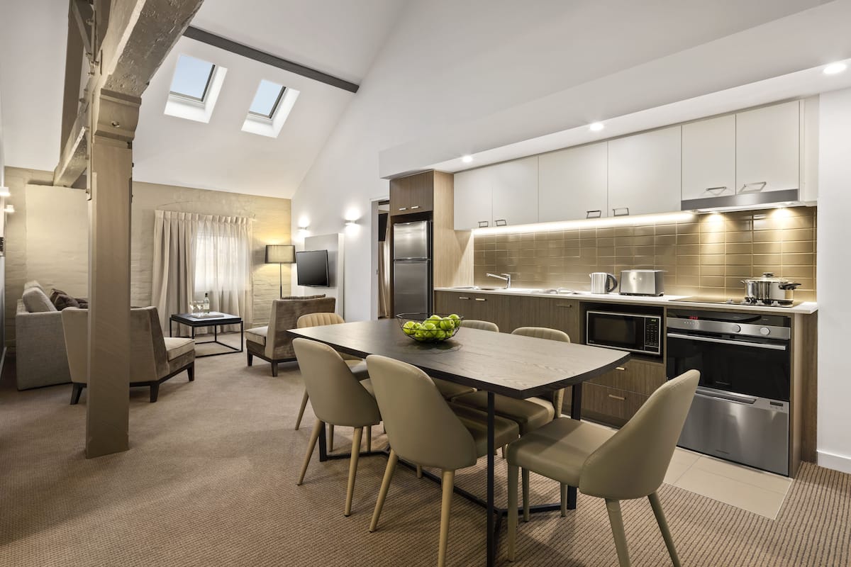 A modern kitchen with a dining area, featuring a large table, chairs, and a bowl of fruit.