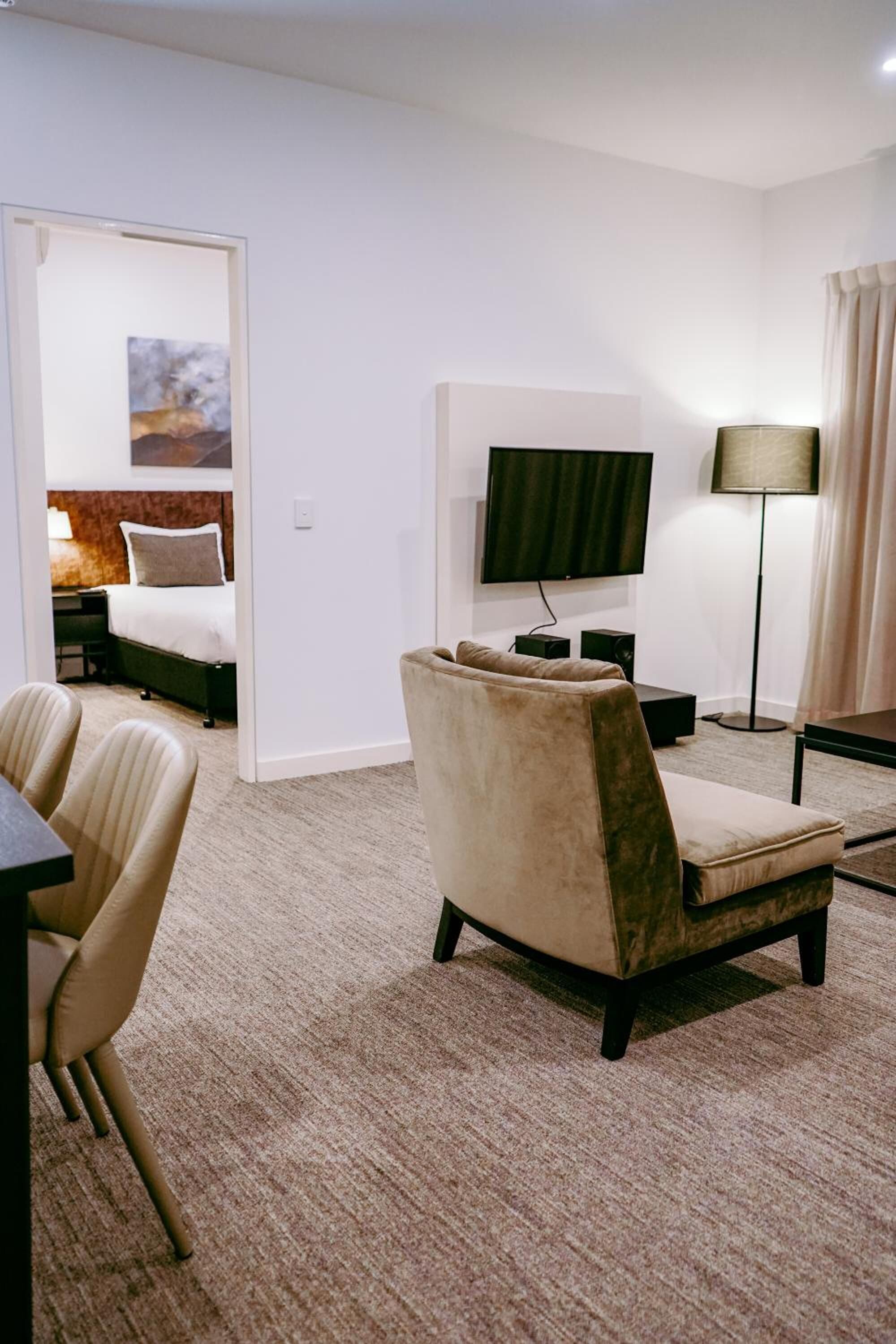 A hotel room with a sofa, a TV, a lamp, and a bed with a painting.