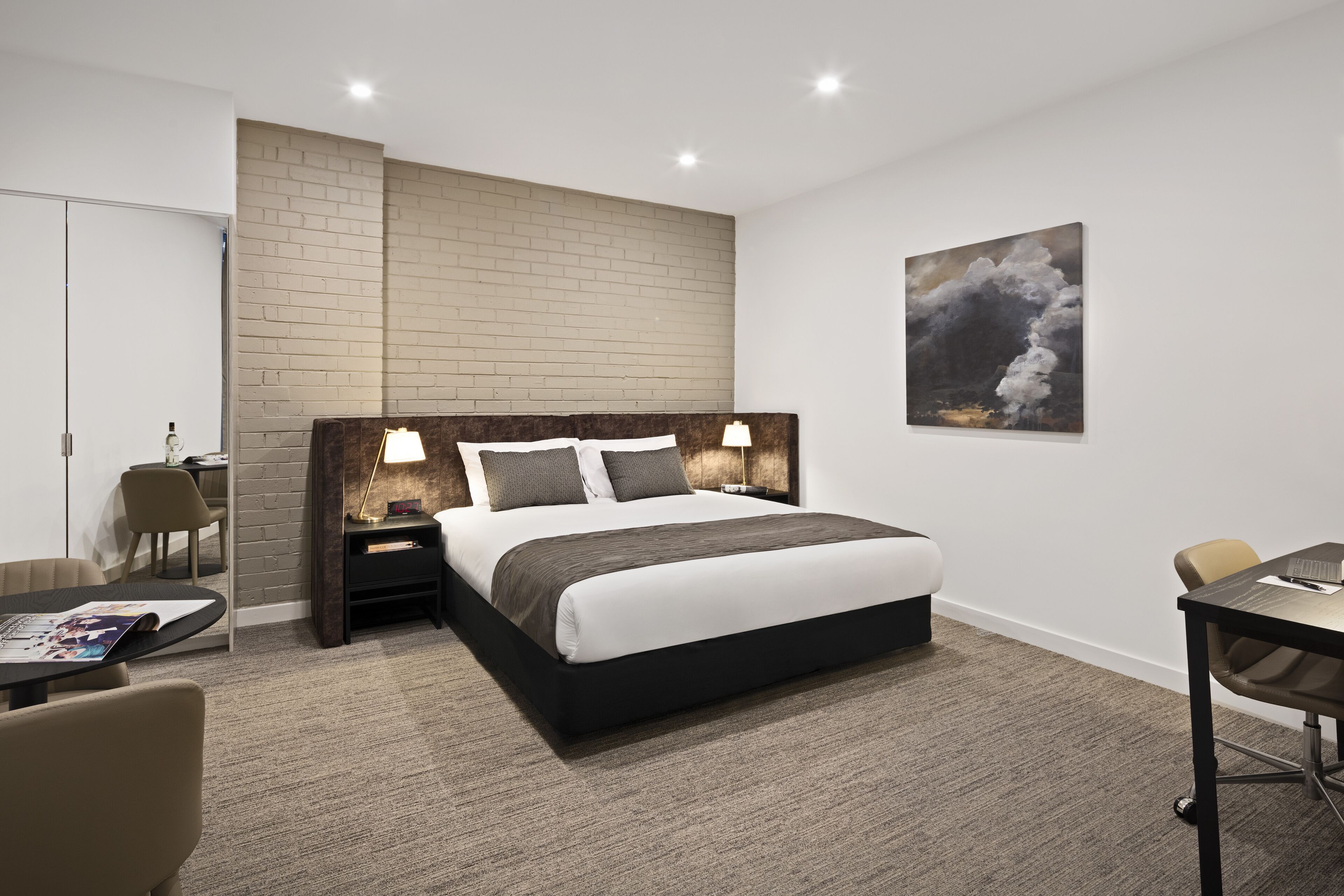 Ein modernes Hotelzimmer mit einem großen Bett, Nachttischen mit Lampen, einem Schreibtisch und einem Stuhl.