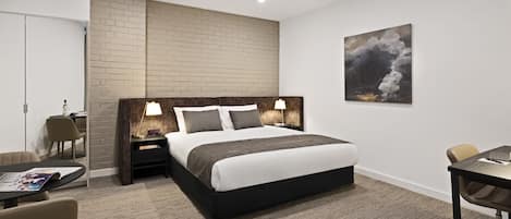 A modern hotel room with a large bed, bedside tables with lamps, a desk, and a chair.