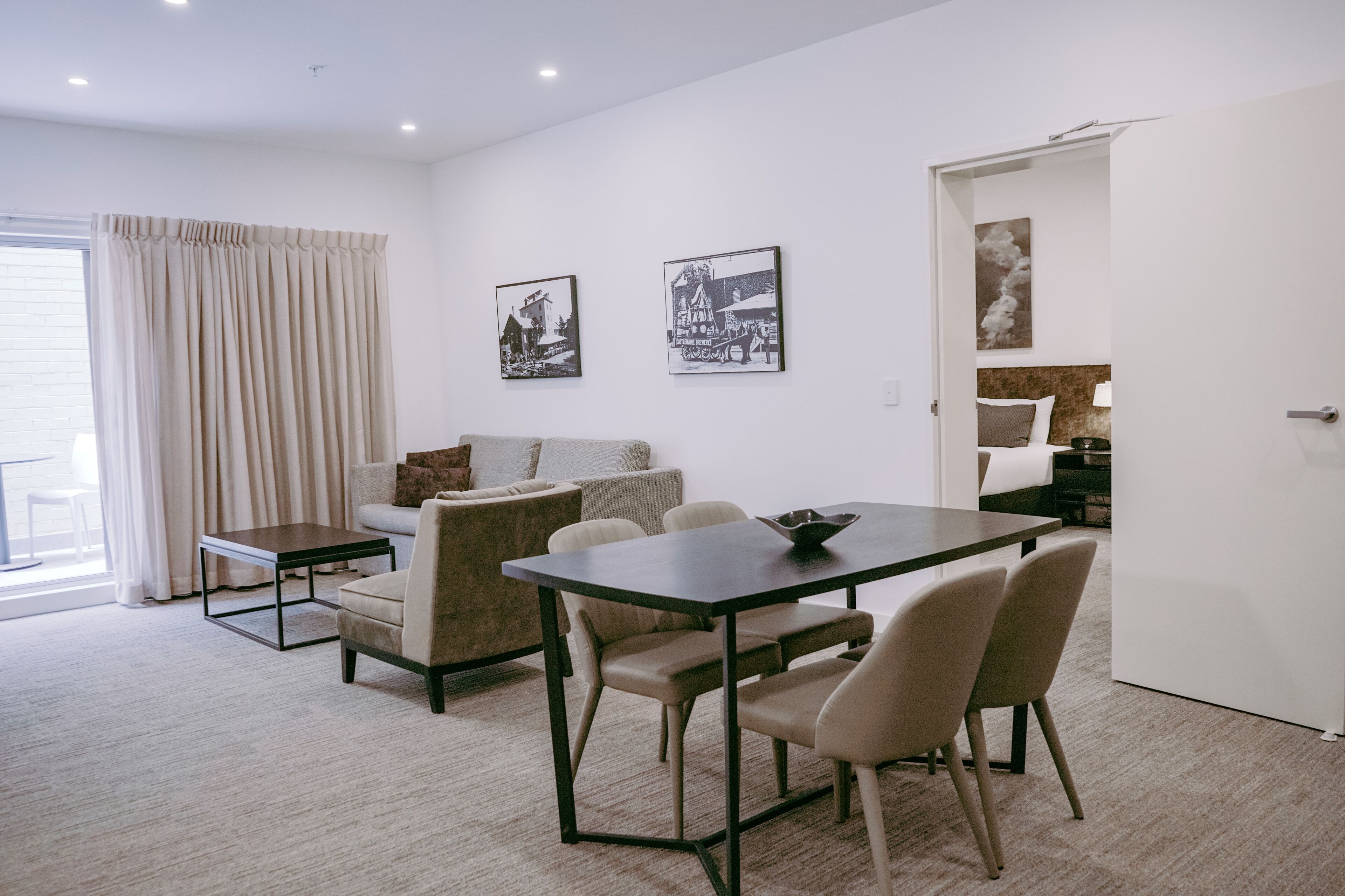 A modern living room with a dining area, a sofa, a coffee table, and a door leading to a bedroom.