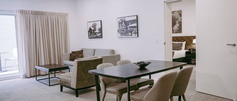 A modern living room with a dining area, a sofa, a coffee table, and a door leading to a bedroom.