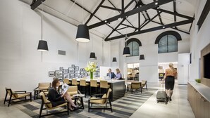 A modern hotel lobby with a reception desk, seating area, and a large window. - Quest Newcastle West (Newcastle West)