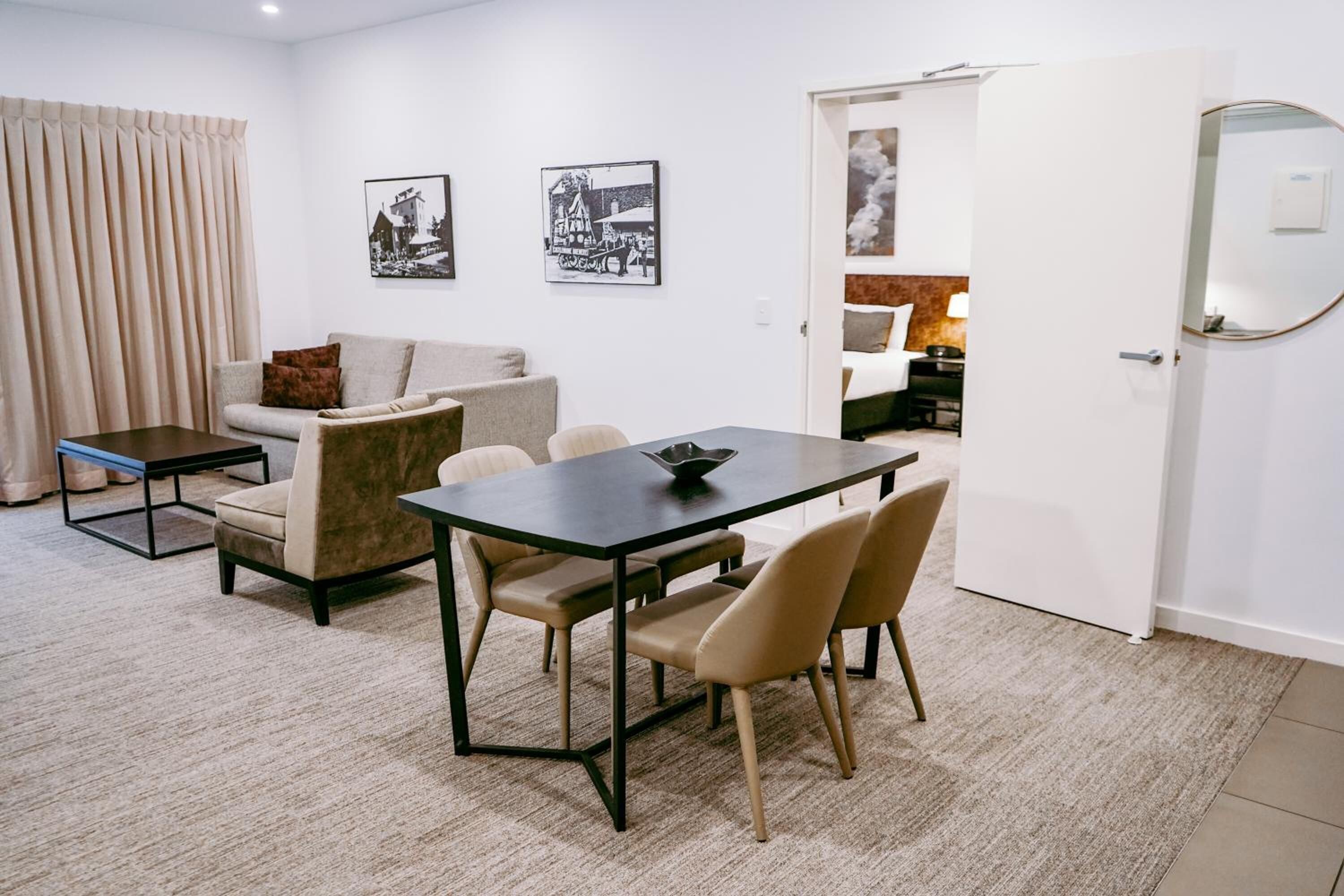 A modern living room with a sofa, a dining table with chairs, a coffee table, and a door leading to a bedroom.