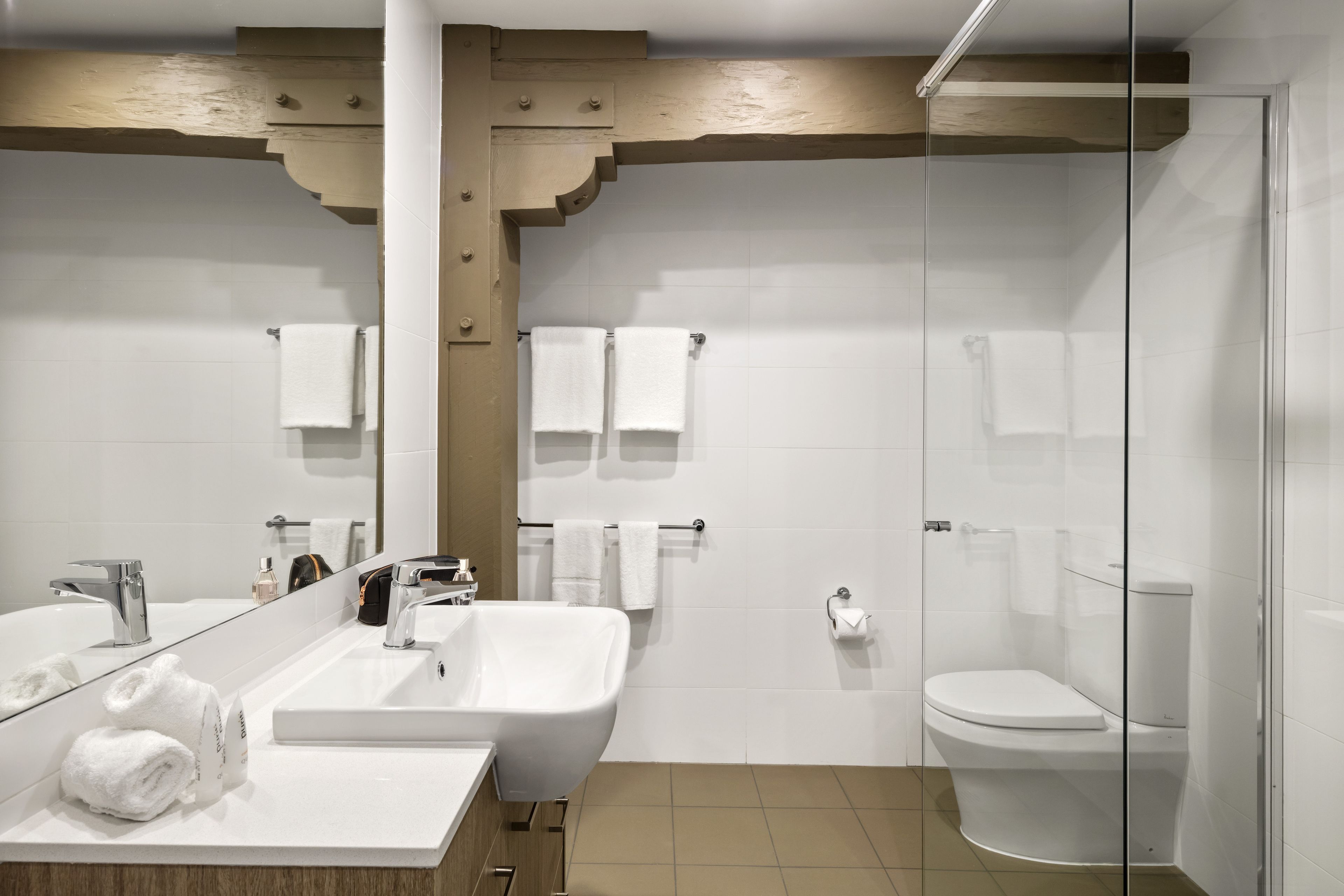 A modern bathroom with a large mirror, two sinks, a shower, and a toilet.